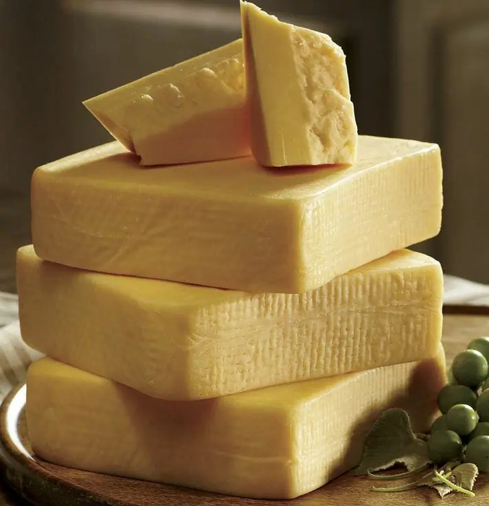 Three stacked blocks of Havarti cheese, with Havarti chunks on top and green grapes on the side.