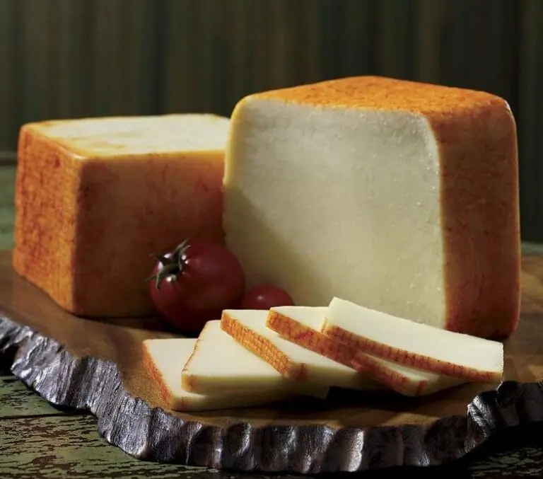 Two blocks and slices of Muenster cheese displayed on a wood slab with cherry tomatoes for garnish.