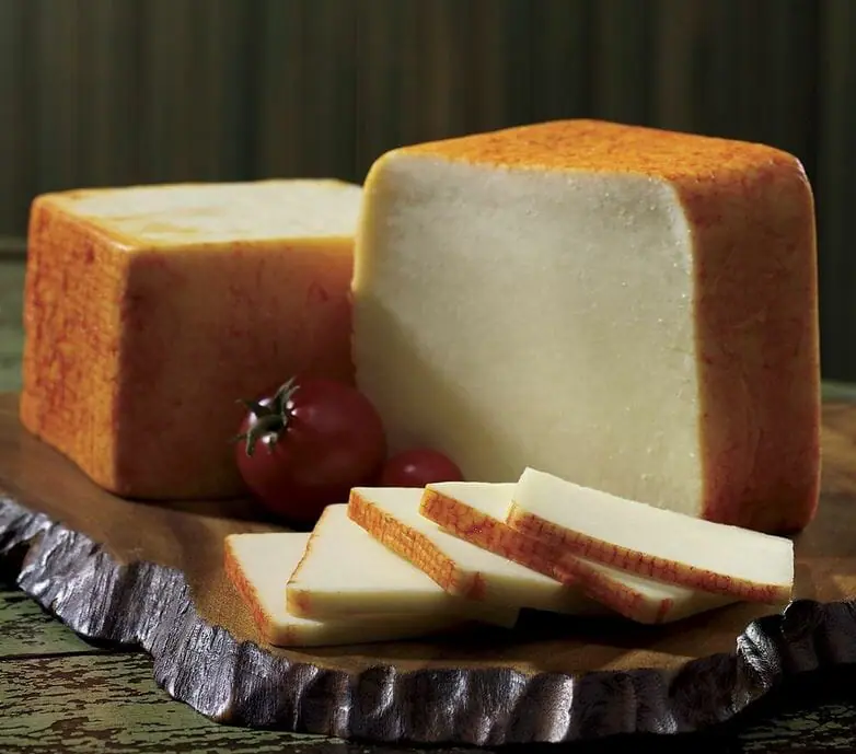 Two blocks and slices of Muenster cheese displayed on a wood slab with cherry tomatoes for garnish.