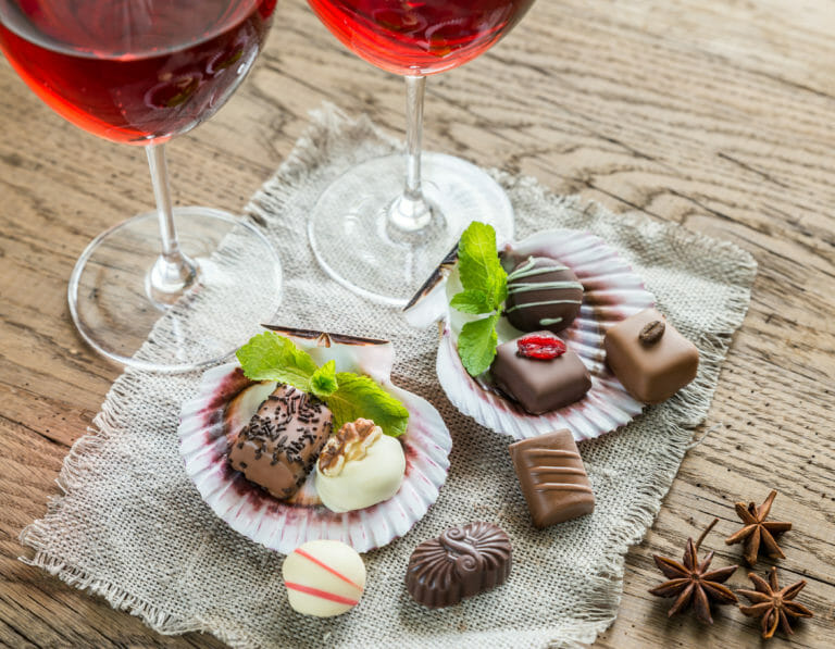 A variety of luxury chocolate candies with two glasses of red wine.
