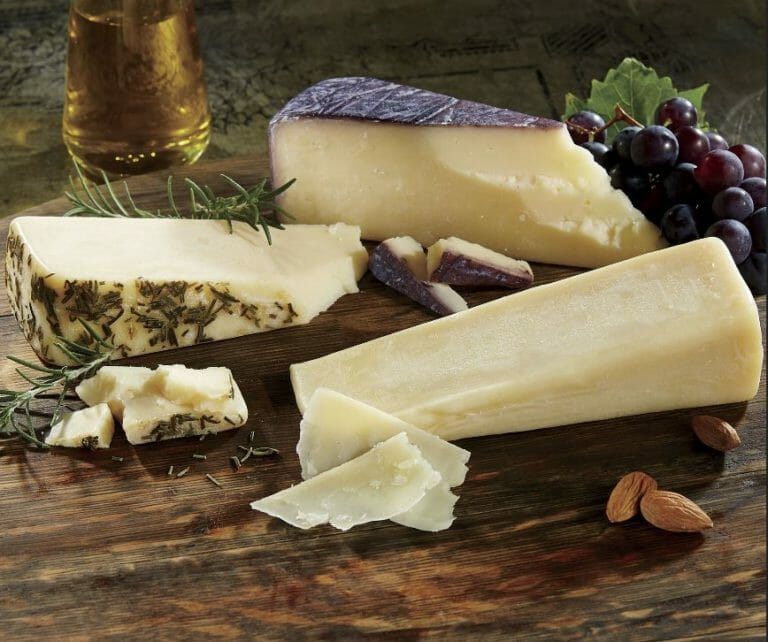 Three varieties of Sartori cheese wedges and pieces with purple grapes, rosemary sprigs and almonds for garnish.