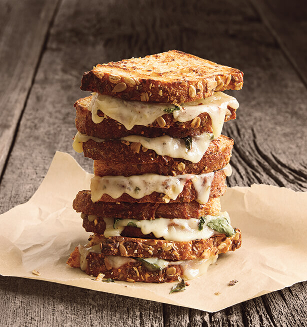 A stack of grilled cheese sandwiches made with hearty seeded bread and melted white cheese mixed with herbs.