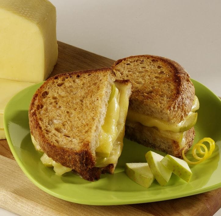 A grilled Havarti cheese and pear sandwich served on a lime green plate with fresh pear wedges for garnish.