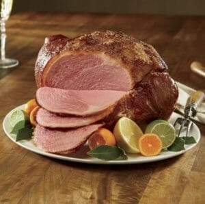 A seasoned ham with slices on a platter with citrus halves and leaves for a Holiday showpiece.