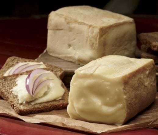 Two blocks of Limburger cheese next to two rye bread slices topped with Limburger and red onion slivers.