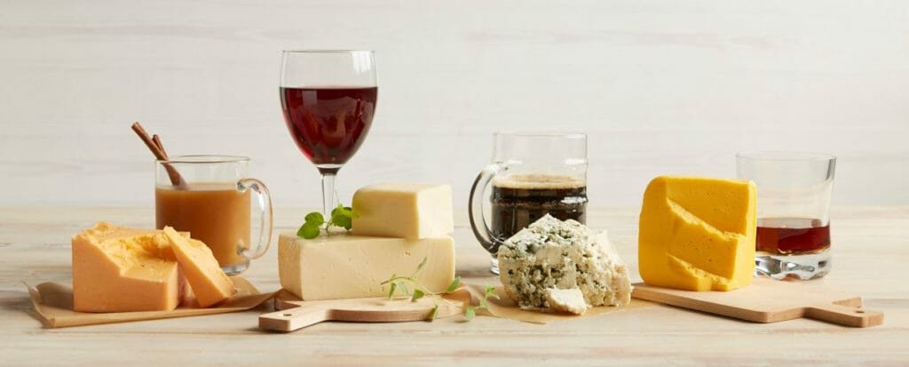 A pairings flight of four cheese varieties with glasses and mugs of mulled cider, red wine, and two kinds of beer.