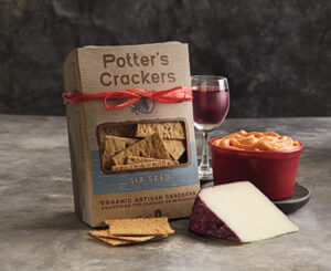 A package of Potter's Crackers next to a tub of Port Wine cheese spread, a wedge of cheese, and a glass of wine.