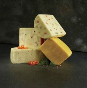 A stacked variety of four different blocks of cheese with sliced red pepper garnish.
