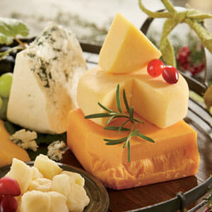 A variety of four cheeses displayed for wine pairings, garnished with red and green grapes and a sprig of rosemary.