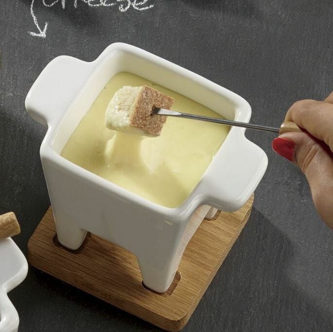 A white ceramic tub of white cheese fondue with a fondue fork dipping a chunk of bread.
