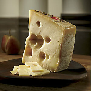 An Emmentaler cheese wedge and slices on a dark wood display board.