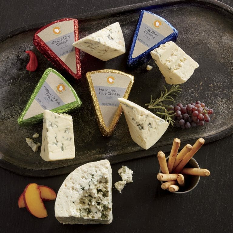 Wedges of an assortment of Blue cheese with grapes, peach slices and breadsticks on a metal serving tray.