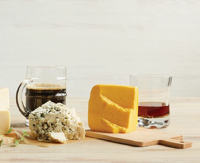Two glass mugs of differents beers with cheddar and blue cheese on a cutting board for beer and cheese pairings.