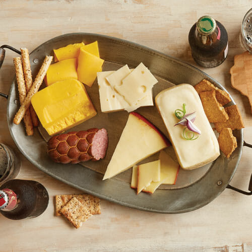 Beer bottles and a metal platter displaying a variety of cheese, sausage and crackers for beer and cheese pairings.metal platter displaying a variety of cheese, sausage and crackers for beer and cheese pairings.