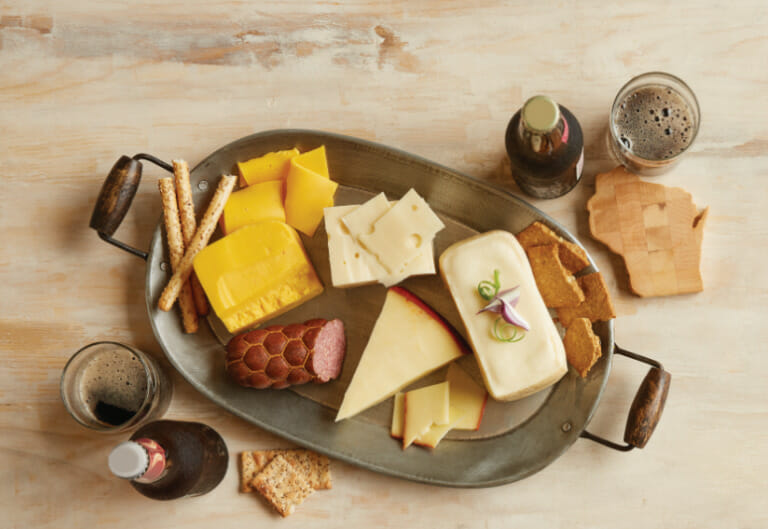 Beer glasses and a metal platter displaying a variety of cheese, sausage and crackers for beer and cheese pairings.metal platter displaying a variety of cheese, sausage and crackers for beer and cheese pairings.