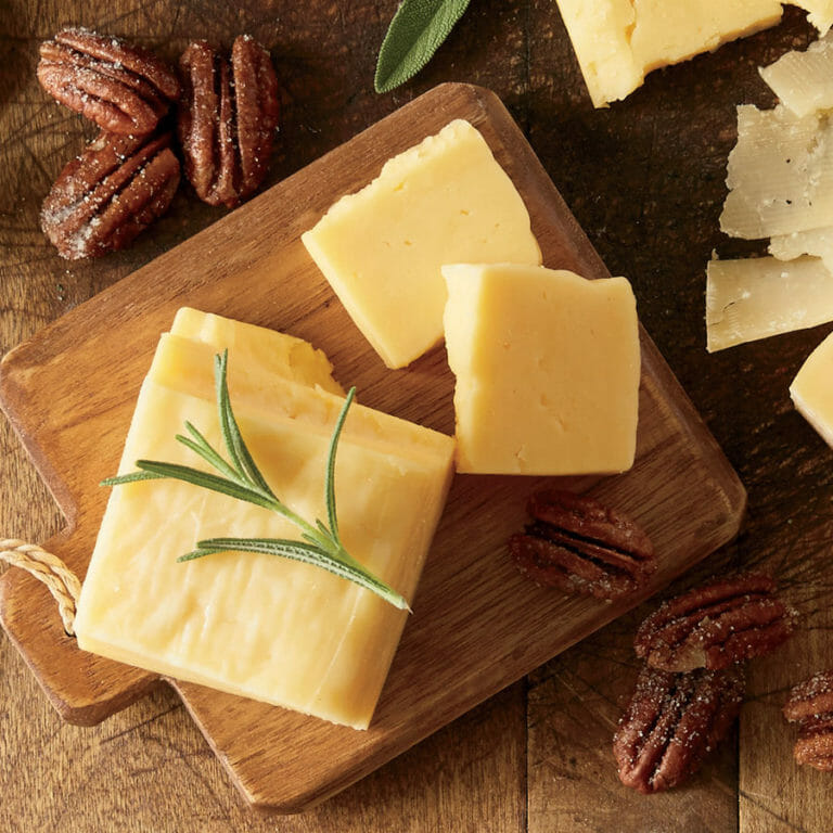 A wooden serving board with pieces of cheese, sugared pecans, and an herb garnish for cheese and nuts pairing.