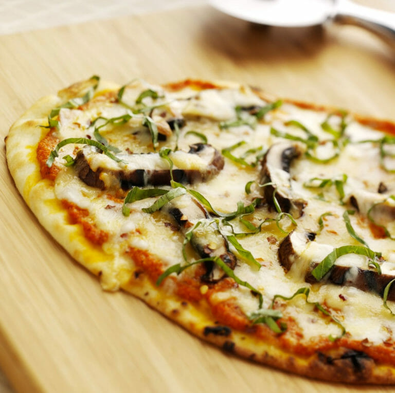 Flatbread mushroom and Mozzarella cheese pizza on a wooden cutting board.